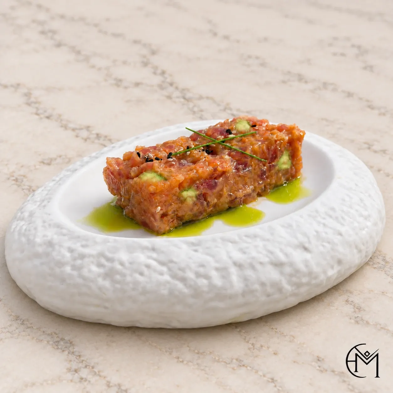 A rectangle of tartare with a fine green garnish and drops of herb oil on a textured white plate.