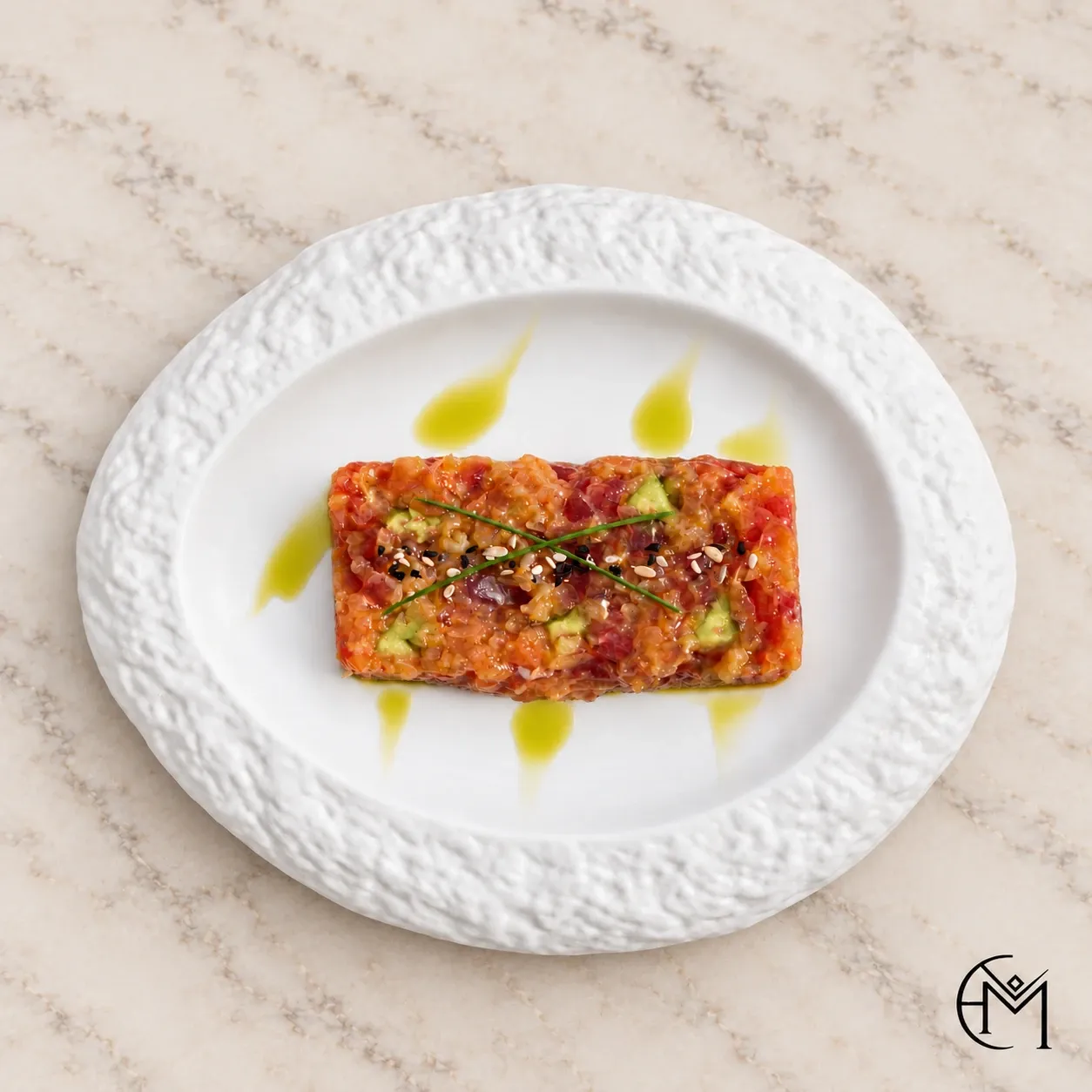 Overhead view of a rectangle of tartare with drops of herb oil on a textured white plate.