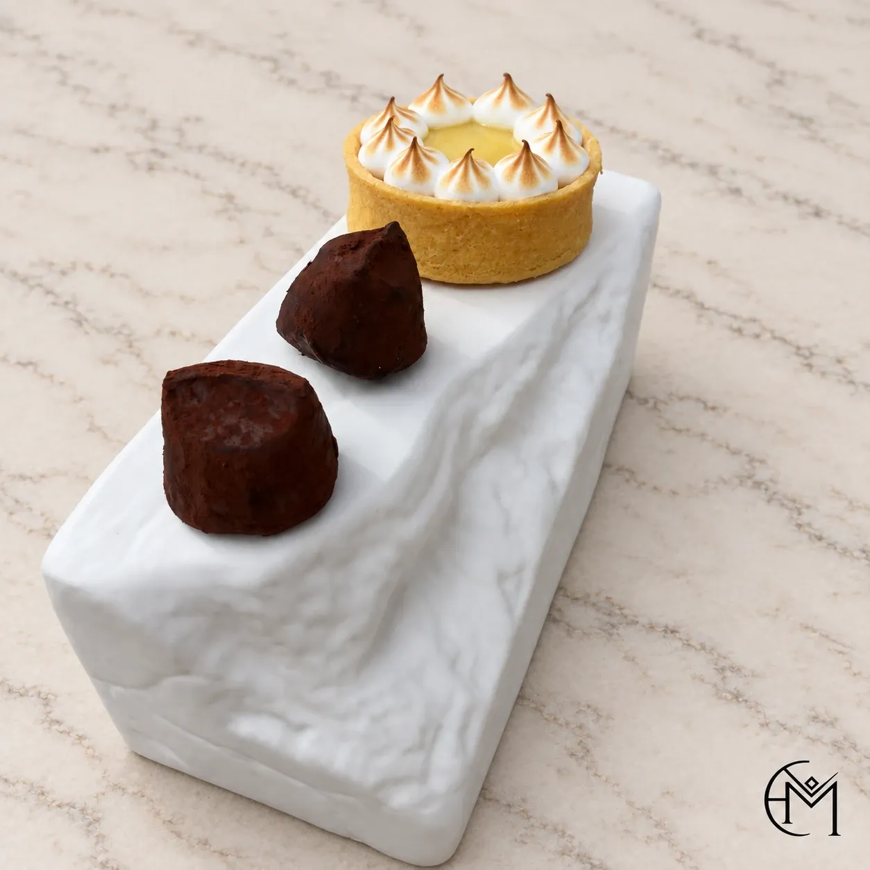 A lemon meringue tartlet and two chocolate truffles on a narrow white plate.